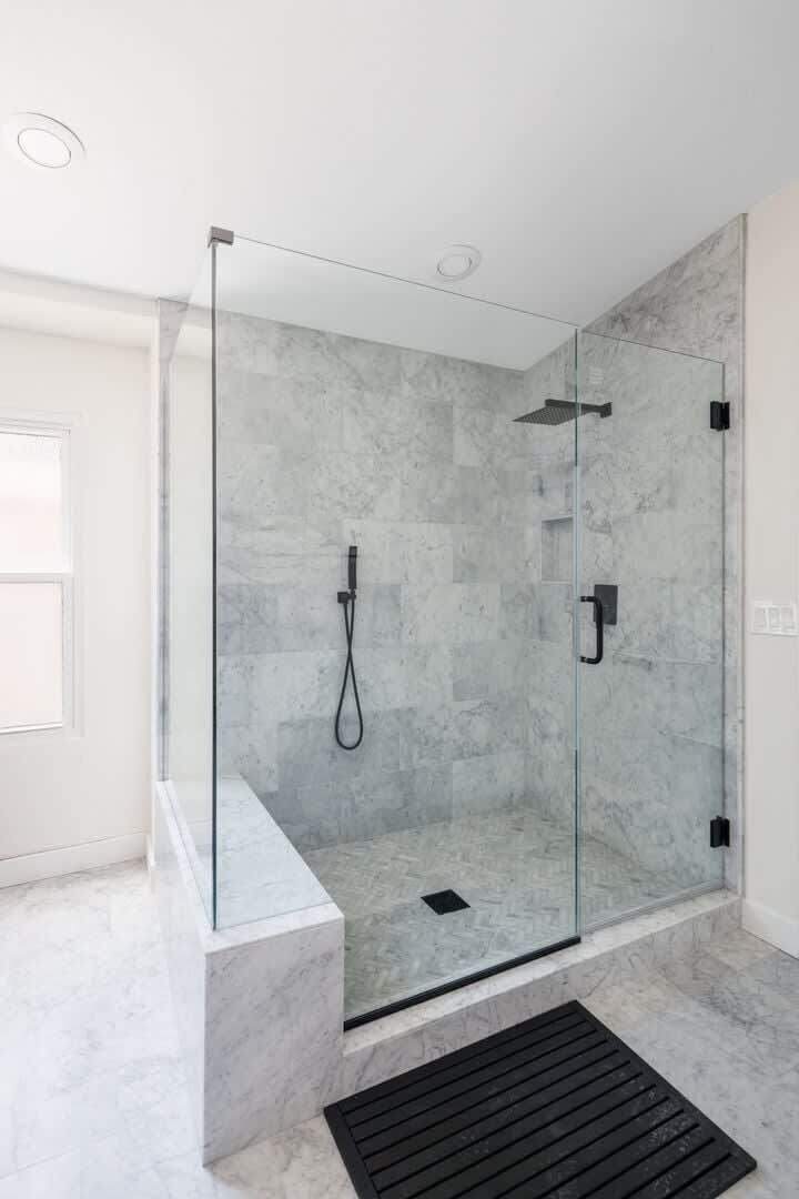 A modern bathroom with a glass-enclosed shower, marble flooring, and a black drain.