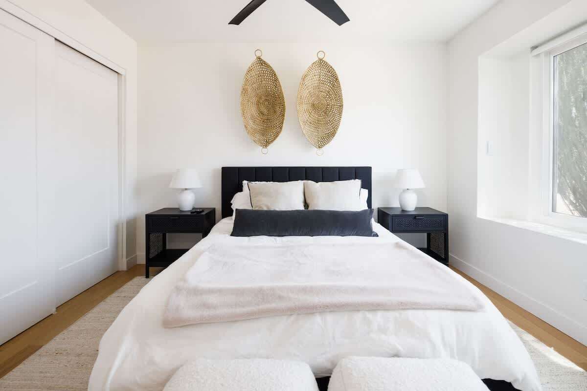 Een moderne slaapkamer met een groot bed, twee nachtkastjes met lampen, een plafondventilator en een groot raam.
