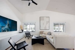 Ein modernes Wohnzimmer mit einem weißen Sofa, einem schwarzen Couchtisch, einem schwarzen Sessel und einem großen, abstrakten Gemälde an der Wand.