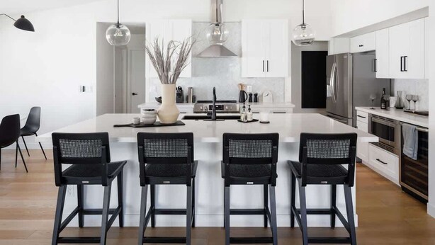 A modern kitchen with a central island, black bar stools, stainless steel appliances, and pendant lighting.