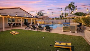 A backyard with a pool, outdoor seating, a grill, and string lights.