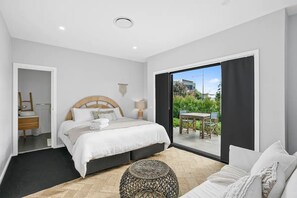 A modern bedroom with a large bed, a small table, and a view of the outdoors.