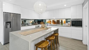 A modern kitchen with white cabinetry, a central island with stools, stainless steel appliances, and a unique spherical pendant light.