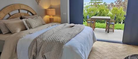 Een slaapkamer met een groot bed, een bedlampje en uitzicht op een terras met een tafel en stoelen.
