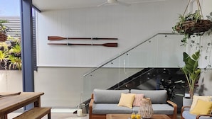 A modern living room with a sofa, coffee table, and wooden bench. There is a ceiling fan, a staircase, and a window with a view of the outdoors.