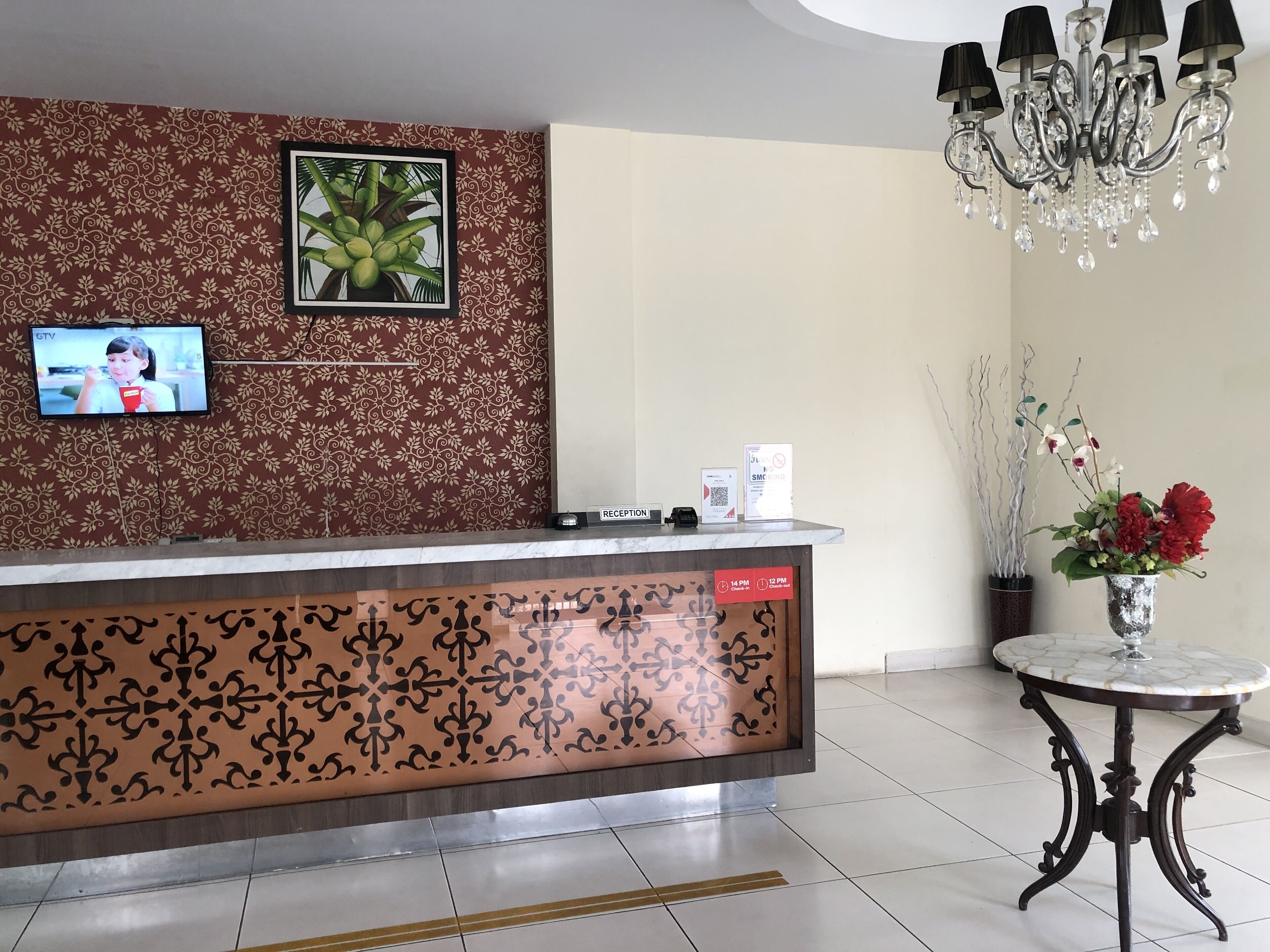 A reception area with a patterned backdrop, a television, a reception desk, a chandelier, and a vase with flowers.