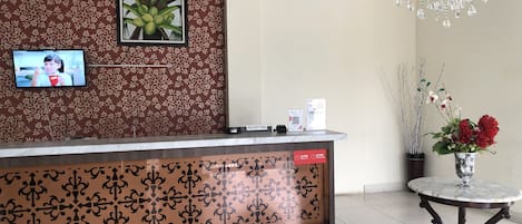 A reception area with a patterned backdrop, a television, a reception desk, a chandelier, and a vase with flowers.