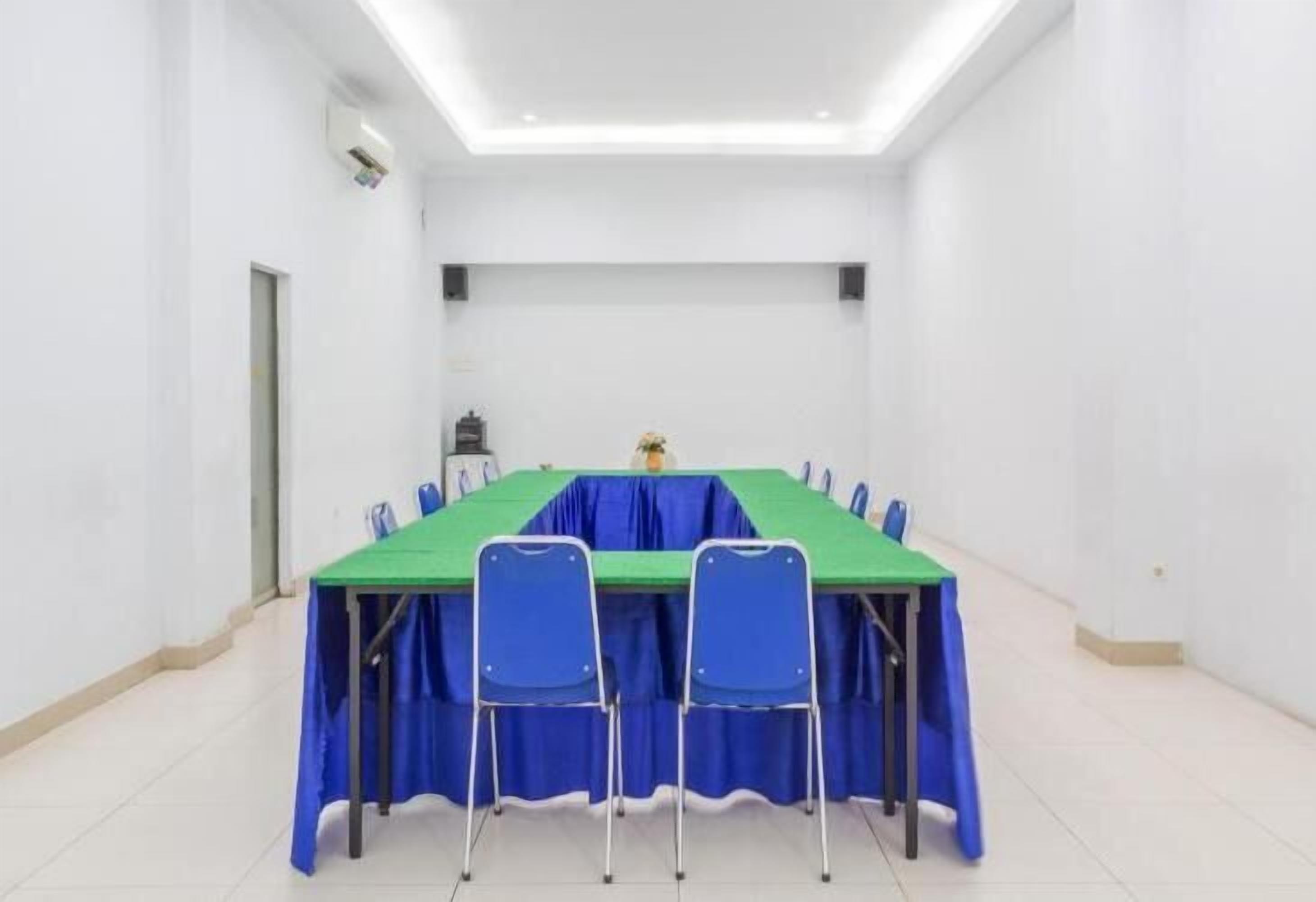 A conference room with a long table, blue chairs, and a green tablecloth.