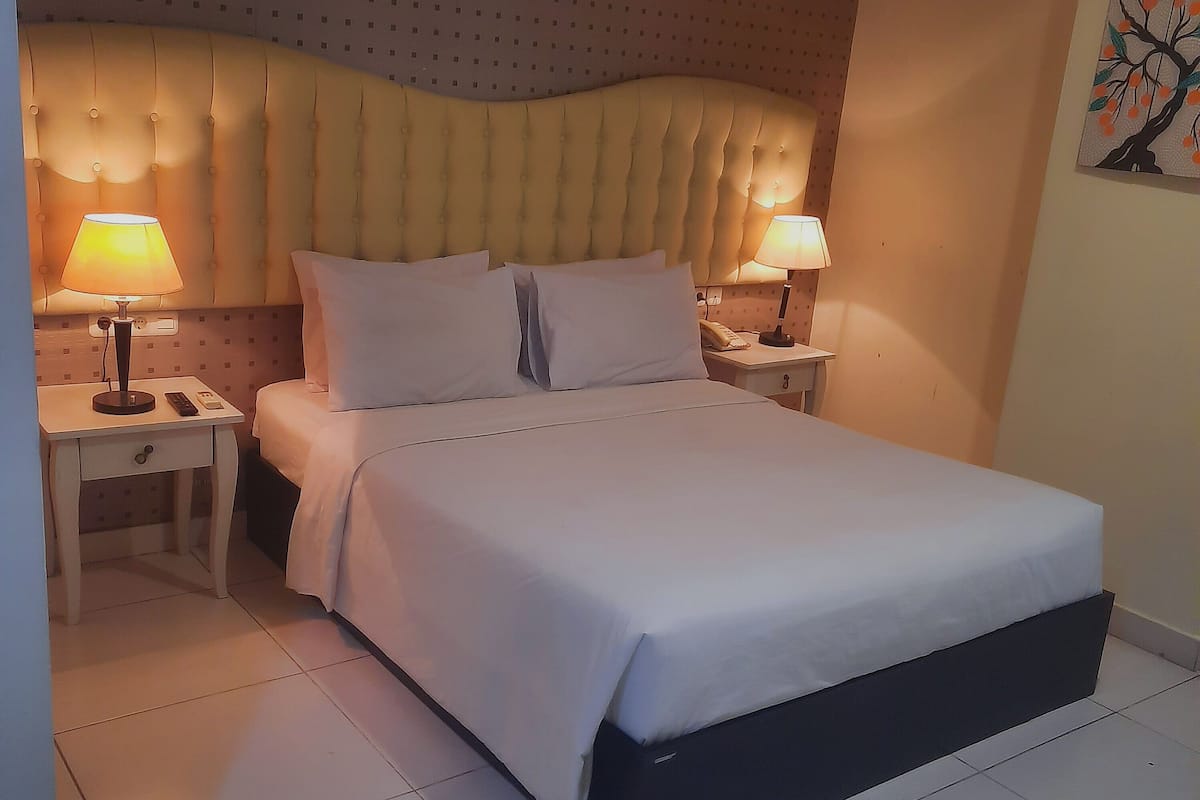 A hotel room with a large bed, two bedside tables with lamps, and a patterned wall.