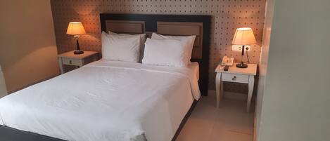 A neatly made bed with white linens, two bedside tables with lamps, and a patterned wall.