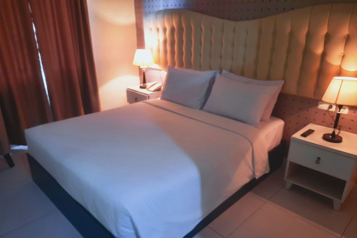 A neatly made bed with white linens, two bedside tables with lamps, and a headboard with a tufted design.