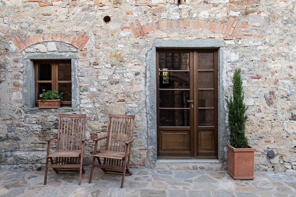 Un bâtiment en pierre avec une porte et une fenêtre en bois, deux chaises en bois et une plante en pot.
