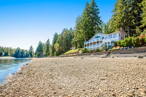 A beachfront property with a large house, a rocky shoreline, and dense forest in the background.