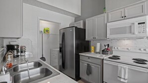 A modern kitchen with stainless steel appliances, a double sink, and white cabinetry. - Cozy 2 Bed 1 Bath Home near IAH (Spring)