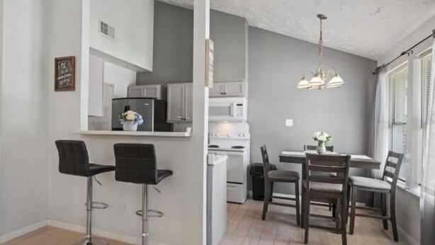 A modern kitchen with white cabinets, a refrigerator, and a dining area with a table and chairs. - Cozy 2 Bed 1 Bath Home near IAH (Spring)