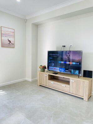 A modern living room with a flat-screen TV on a wooden stand, a framed picture on the wall, and a small plant on the stand. - Luxury Home In Melton South- Free Parking And Wifi !! (Strathtulloh)