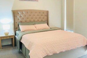 A bedroom with a tufted headboard, a bed with a peach-colored blanket, and a bedside table with a lamp. - Luxury Home In Melton South- Free Parking And Wifi !! (Strathtulloh)