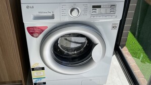 Eine LG Wasch-Trockner-Kombination mit Frontlader, digitalem Display sowie Kennzeichnungen für Energie- und Wasserverbrauch. Auf der Oberseite befindet sich ein weißer Wäschekorb.