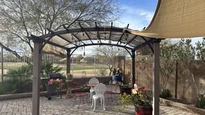 Un patio techado con piso de ladrillo, mobiliario exterior, plantas en macetas y vista a un campo de golf.