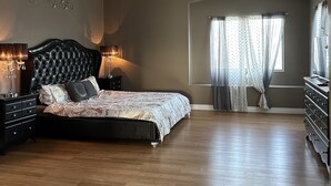 Un dormitorio amplio con una cama grande, un ventilador de techo y una ventana con cortinas.