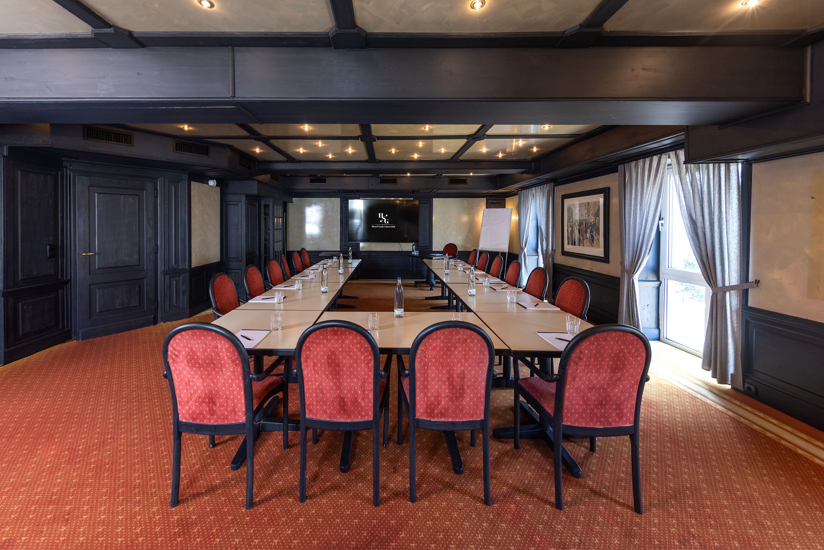 A conference room with a long table, red chairs, and a projector screen.