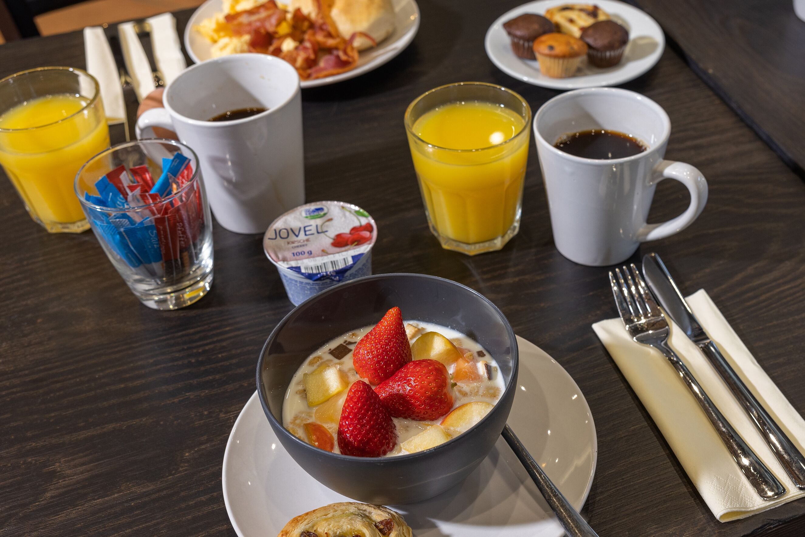 Una mesa de desayuno con un tazón de yogur, un vaso de jugo de naranja y una taza de café.