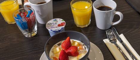 Una mesa de desayuno con un tazón de yogur, un vaso de jugo de naranja y una taza de café.
