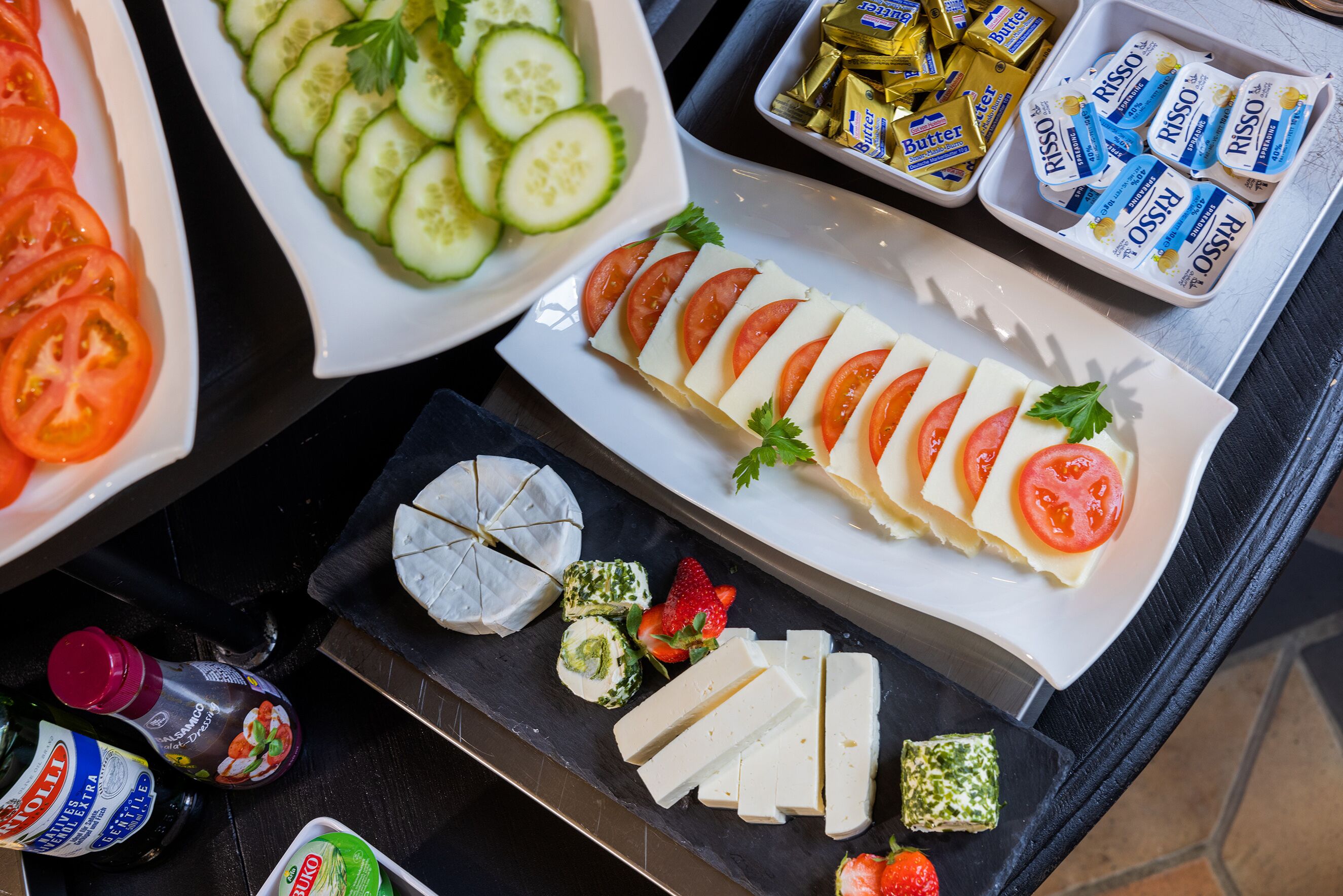 A variety of cheeses, including sliced tomatoes and cucumbers, arranged on a tray.