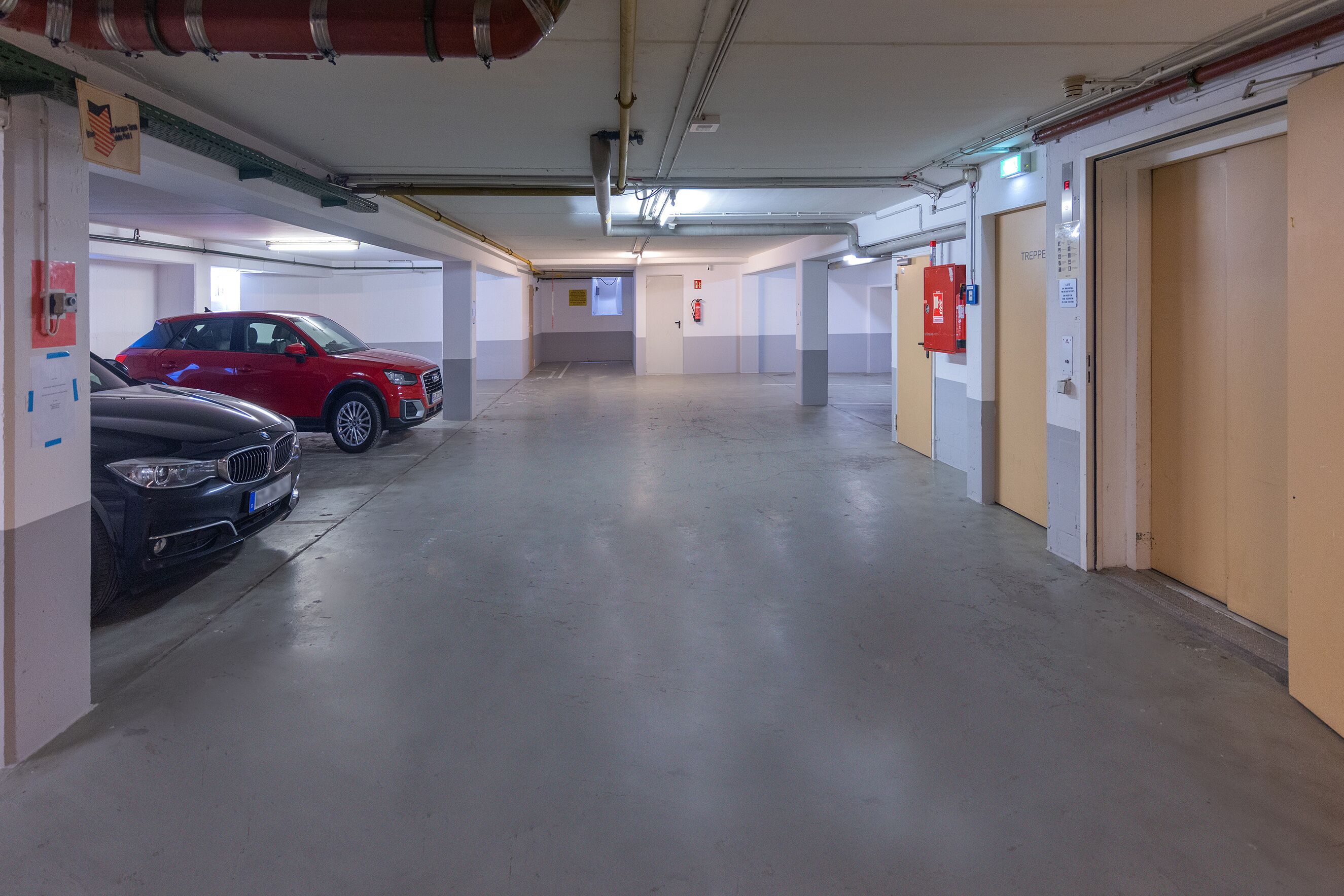 Un estacionamiento de varios niveles con varios coches aparcados, incluyendo un SUV rojo y un sedán negro.