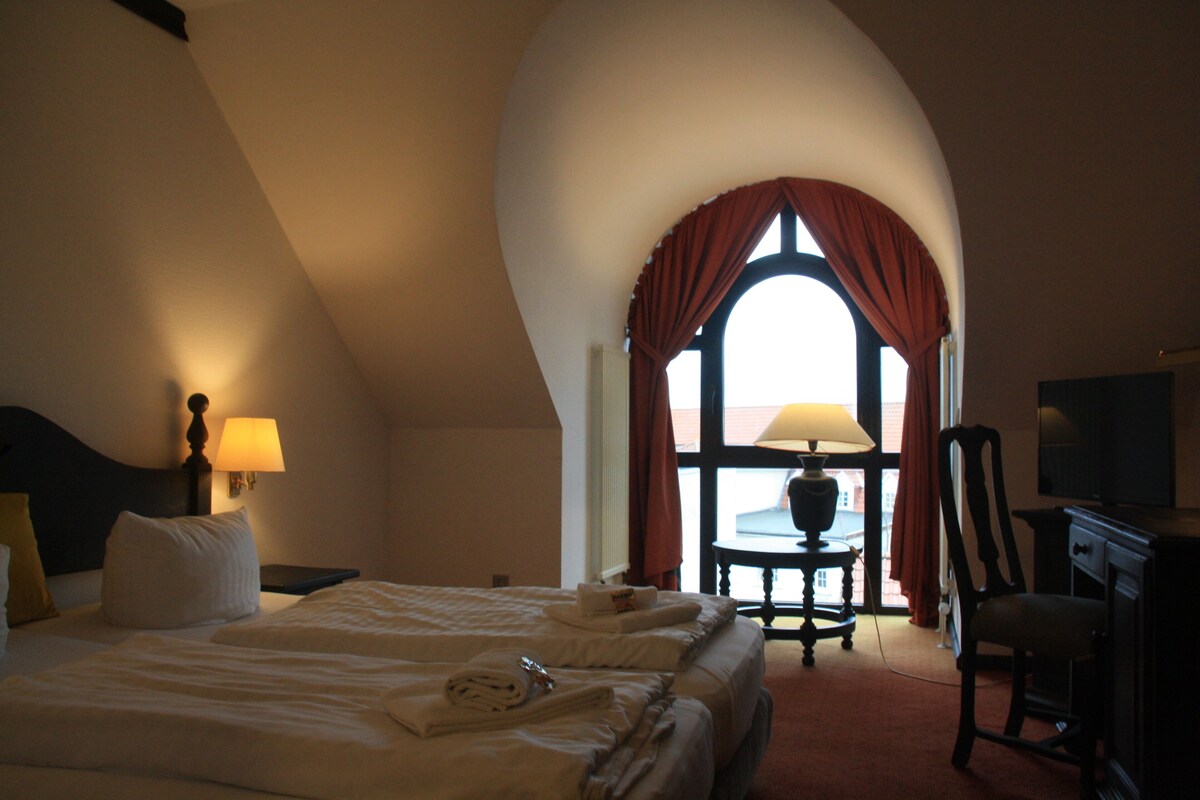 A hotel room with a large bed, a desk, a chair, a television, and a window with curtains.