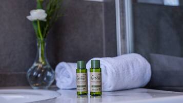 Twee flessen 'Green' haar- en bodywash op een badkamermeubel, met een witte handdoek en een bloemenvaas op de achtergrond.