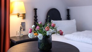 Una habitación de hotel con una cama, una mesita de noche con lámpara y un jarrón con flores sobre una mesa.