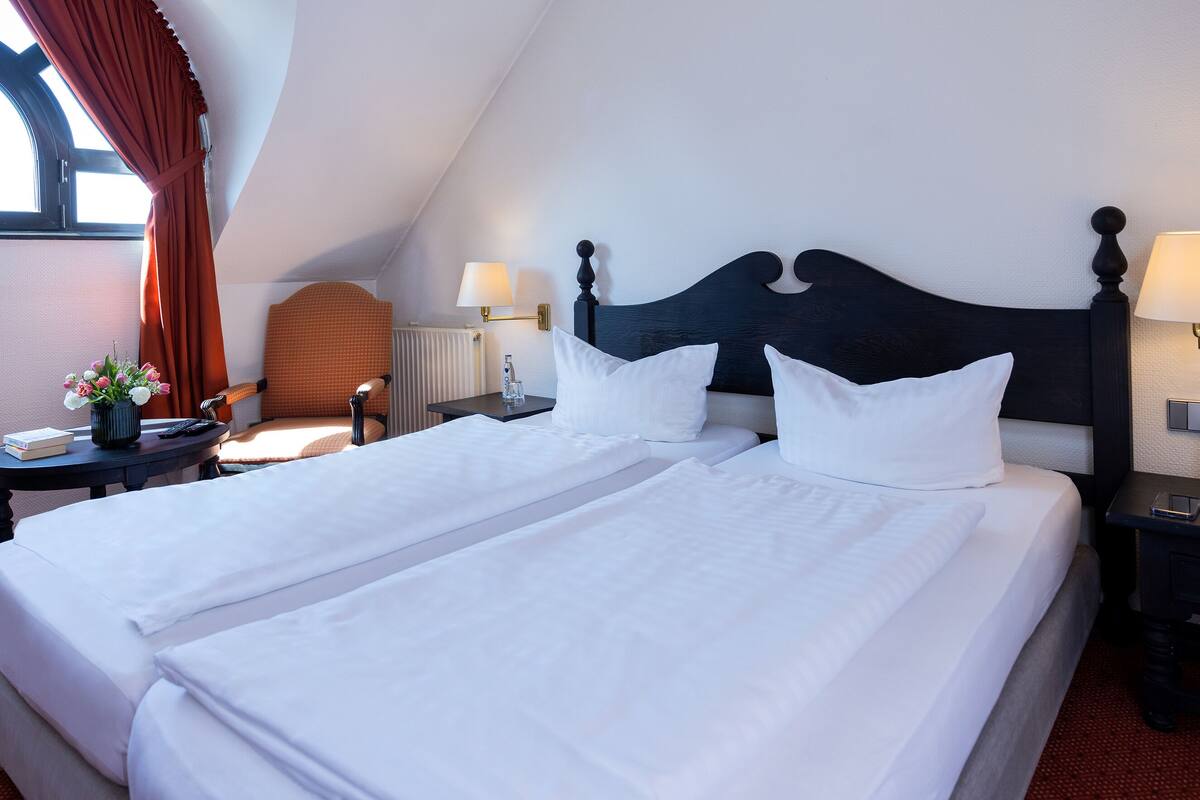 Una habitación de hotel con una cama grande, dos mesitas de noche, una silla y un ventanal con cortinas.