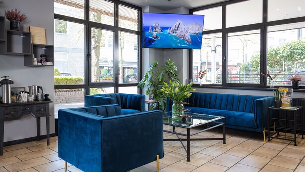 Un moderno vestíbulo de hotel con un sofá azul, una estación de café y una gran pantalla de televisión que muestra una vista panorámica.