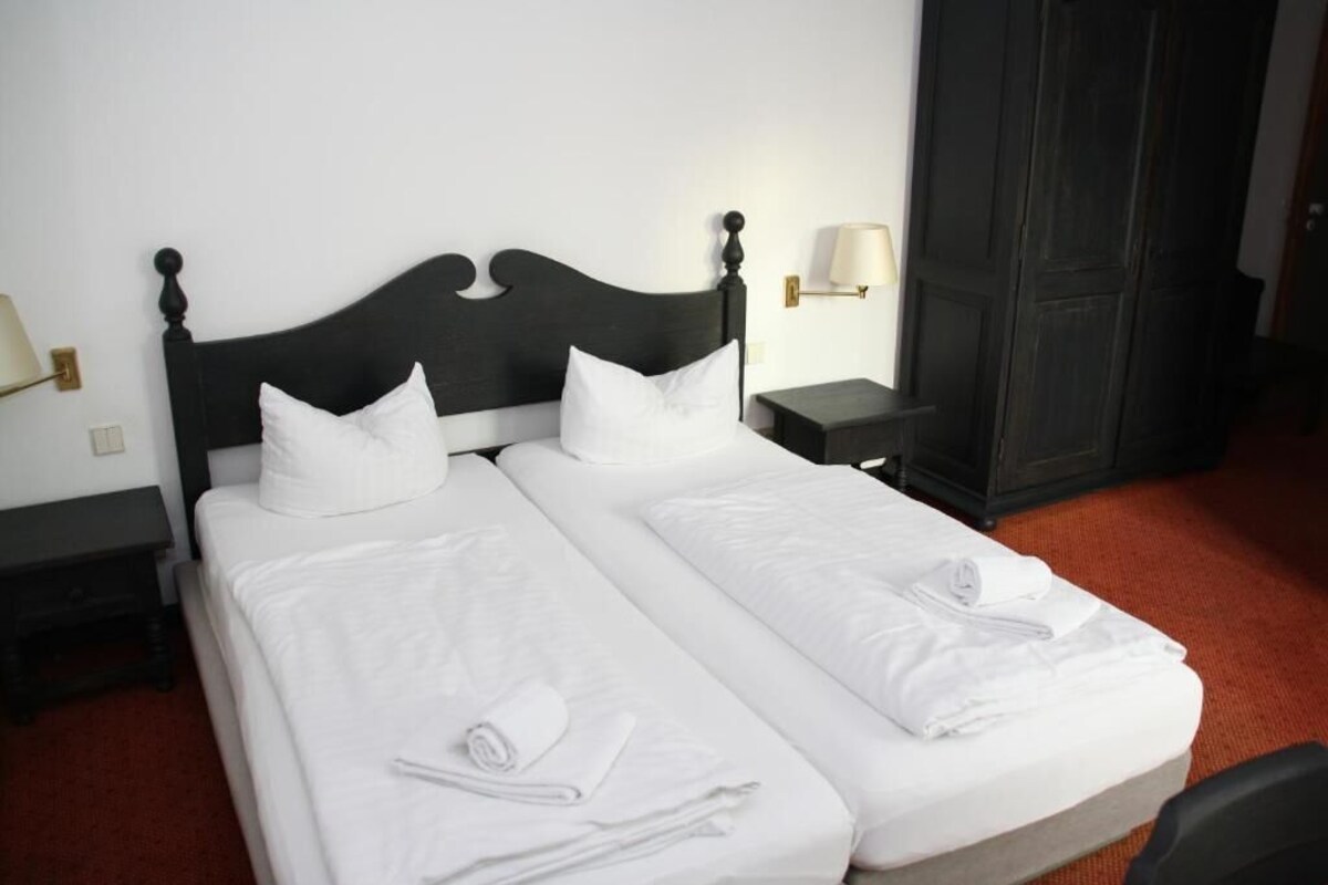 A double bed with white linens and pillows, two bedside tables with lamps, and a dark wooden wardrobe.
