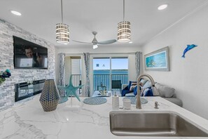 A modern kitchen with a large island, a built-in TV, and a view of the ocean.