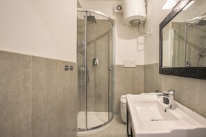 A modern bathroom with a glass-enclosed shower, a white sink, and a large mirror.