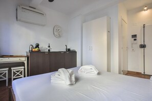 A hotel room with a bed, a desk, a wardrobe, a sink, and an air conditioning unit.