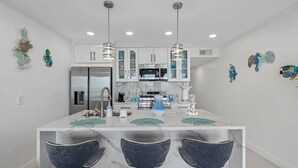 A modern kitchen with white cabinets, a marble island, and three bar stools.