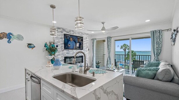 A modern kitchen with a large island, a ceiling fan, and a view of the ocean.