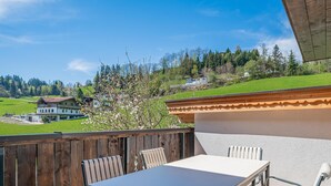 An outdoor patio with a table and chairs, surrounded by a wooden fence, overlooking a green landscape and buildings in the distance.