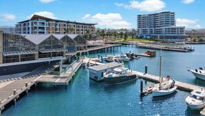 Un port de plaisance avec des bateaux amarrés, un bâtiment moderne doté de grandes fenêtres et une jetée qui s’avance dans l’eau.