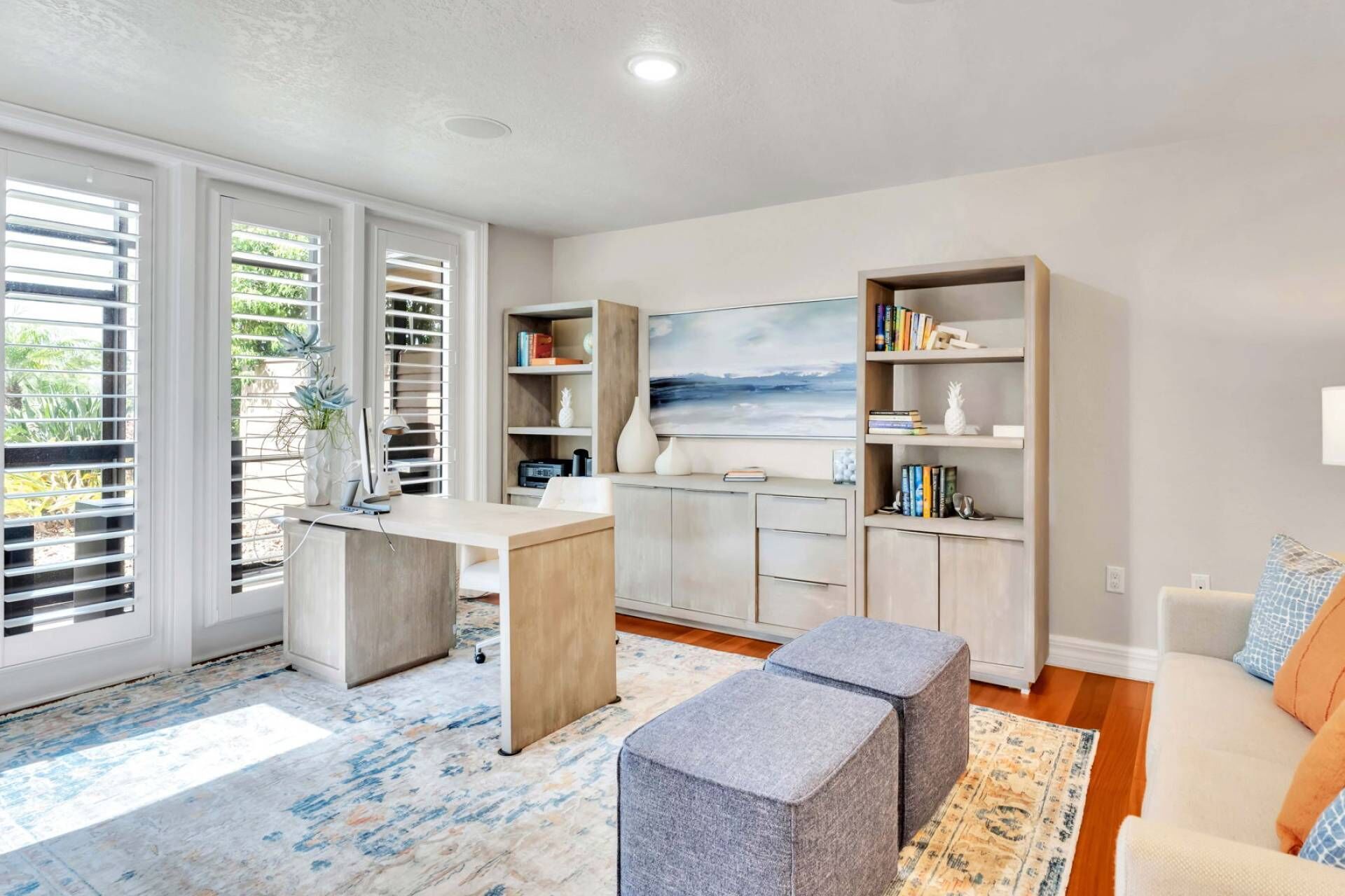 A modern home office with a desk, bookshelves, and a painting.