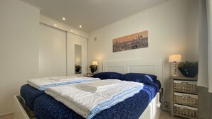 Quarto com uma cama grande, mesa de cabeceira com abajur, espelho e um quadro na parede.