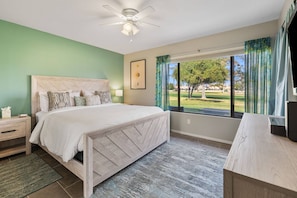 Ein Schlafzimmer mit Bett, Nachttisch und Blick auf einen Golfplatz.