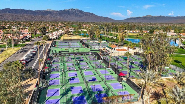 Un complex de pistes de tennis amb diverses pistes, envoltat d'edificis residencials i un paisatge de muntanyes.