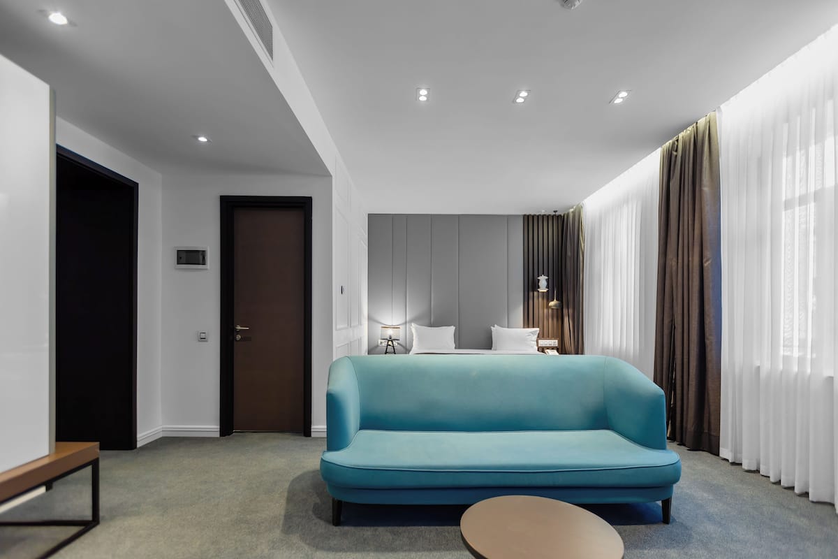 A modern hotel room with a teal sofa, a small round table, and a bed with white linens.