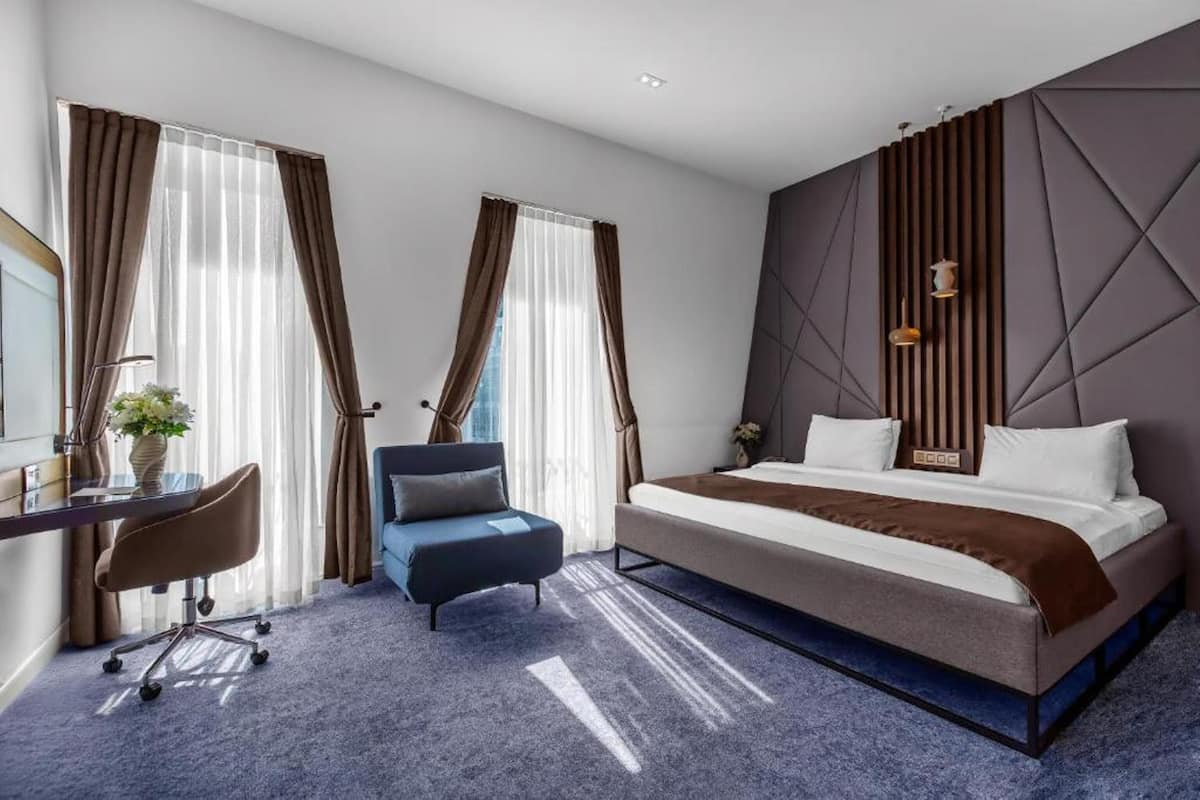 A modern hotel room with a bed, a desk, a chair, and a large window with curtains.