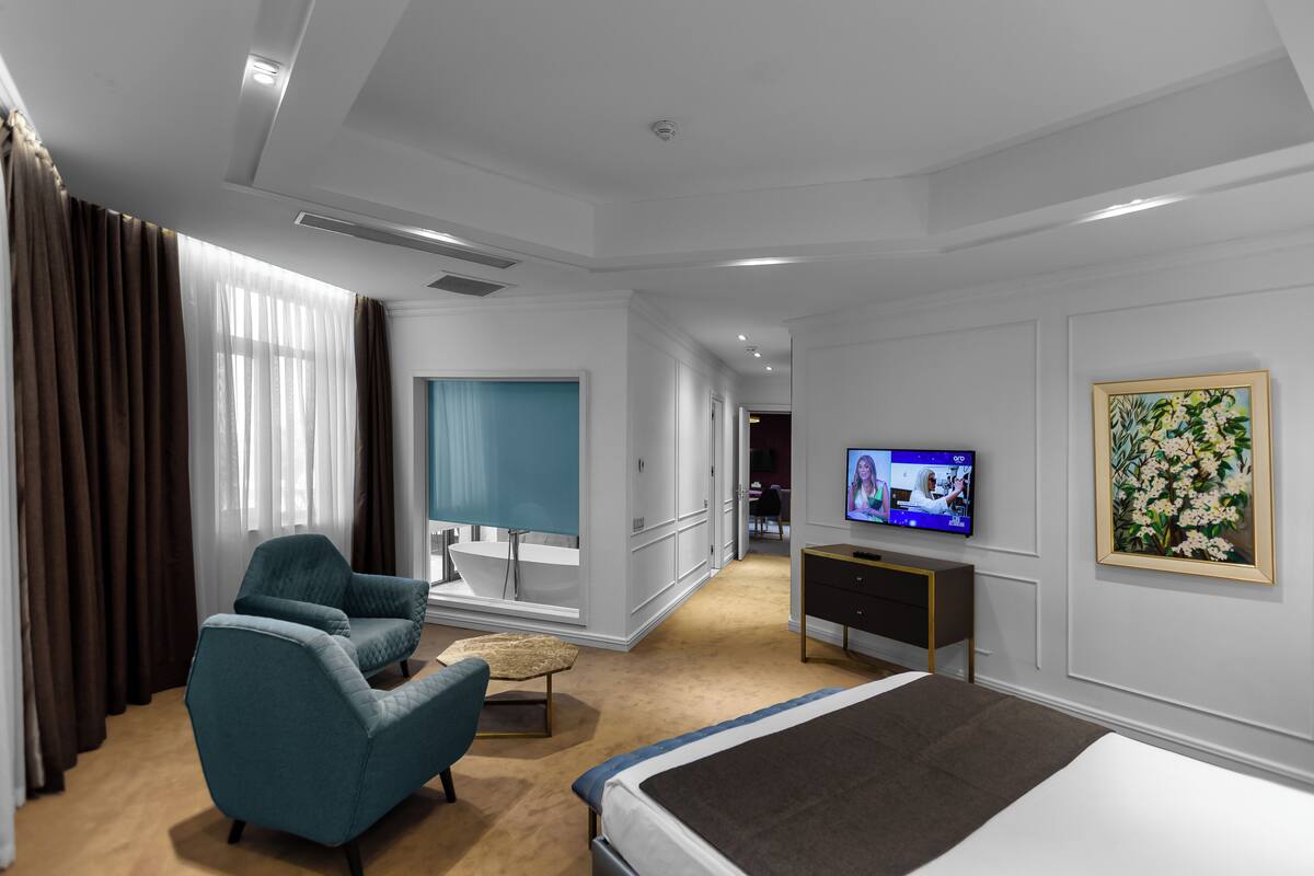 A modern hotel room with a large bed, a television, a desk, and a window with curtains.