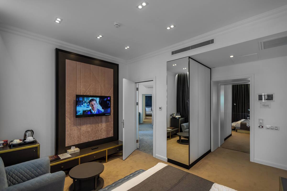 A modern hotel room with a flat-screen TV, a sofa, a coffee table, and a mirror.